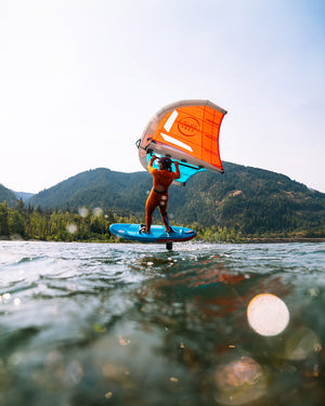 Orange and white kiteboarding sail with blue board on 2025 Above Air inflatable foilboard