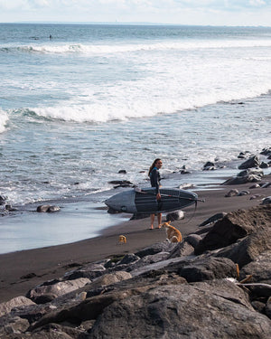 Black fiberglass surfboard with white fins and leash, Spice Paddleboard