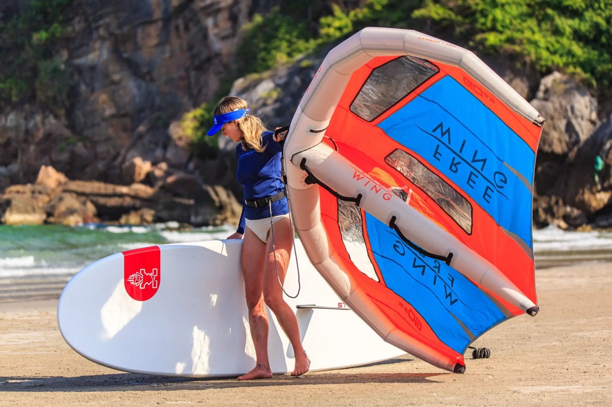 Red and white surfboard with blue leash and orange sail for beginner winging