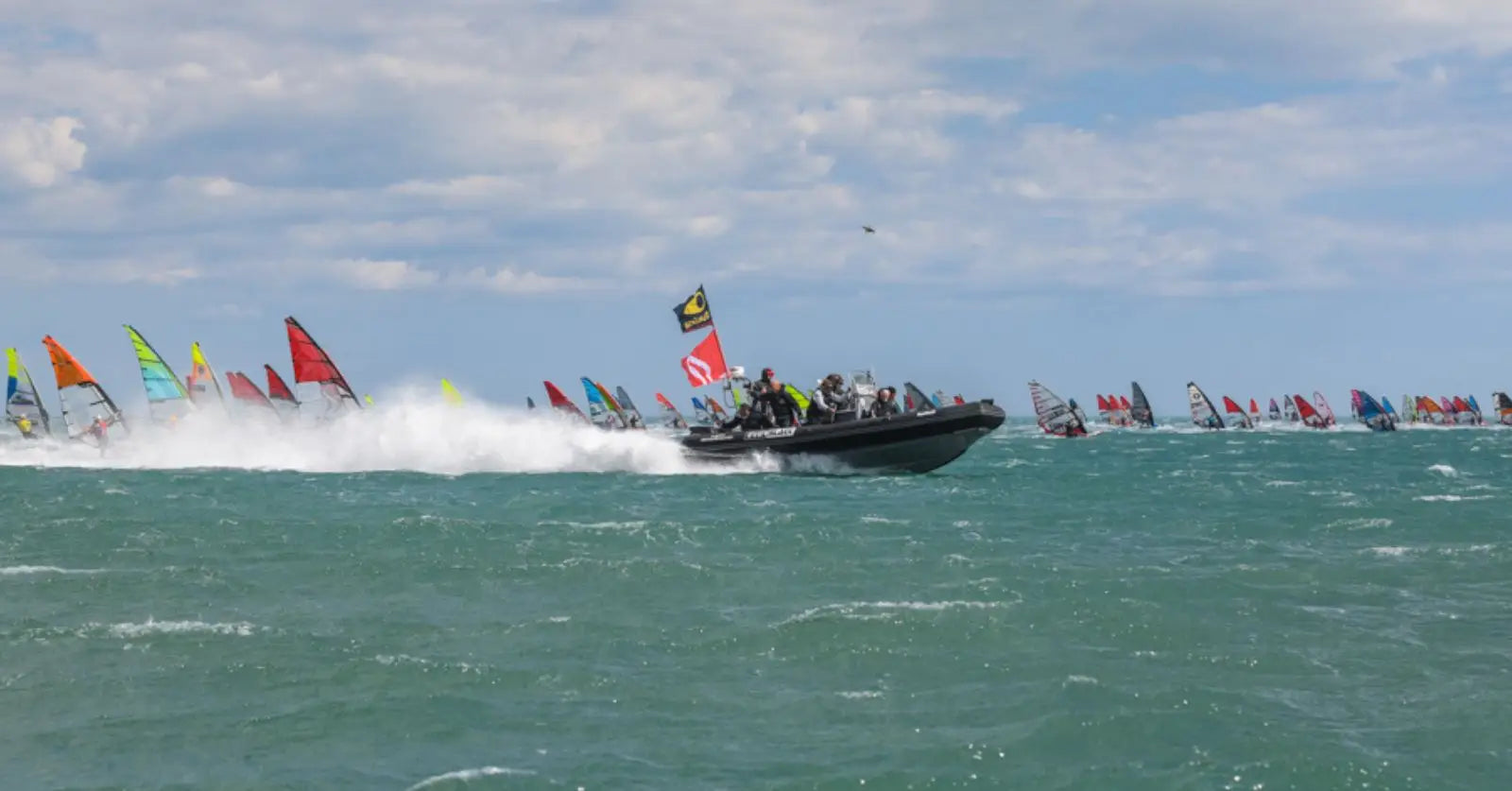 Rigid inflatable boat with colorful flags and black seats for Defi Wind 2025