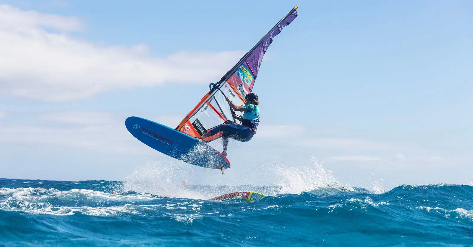 Blue Starboard windsurfing board with purple sail and black harness at PWA Fuerteventura World Cup