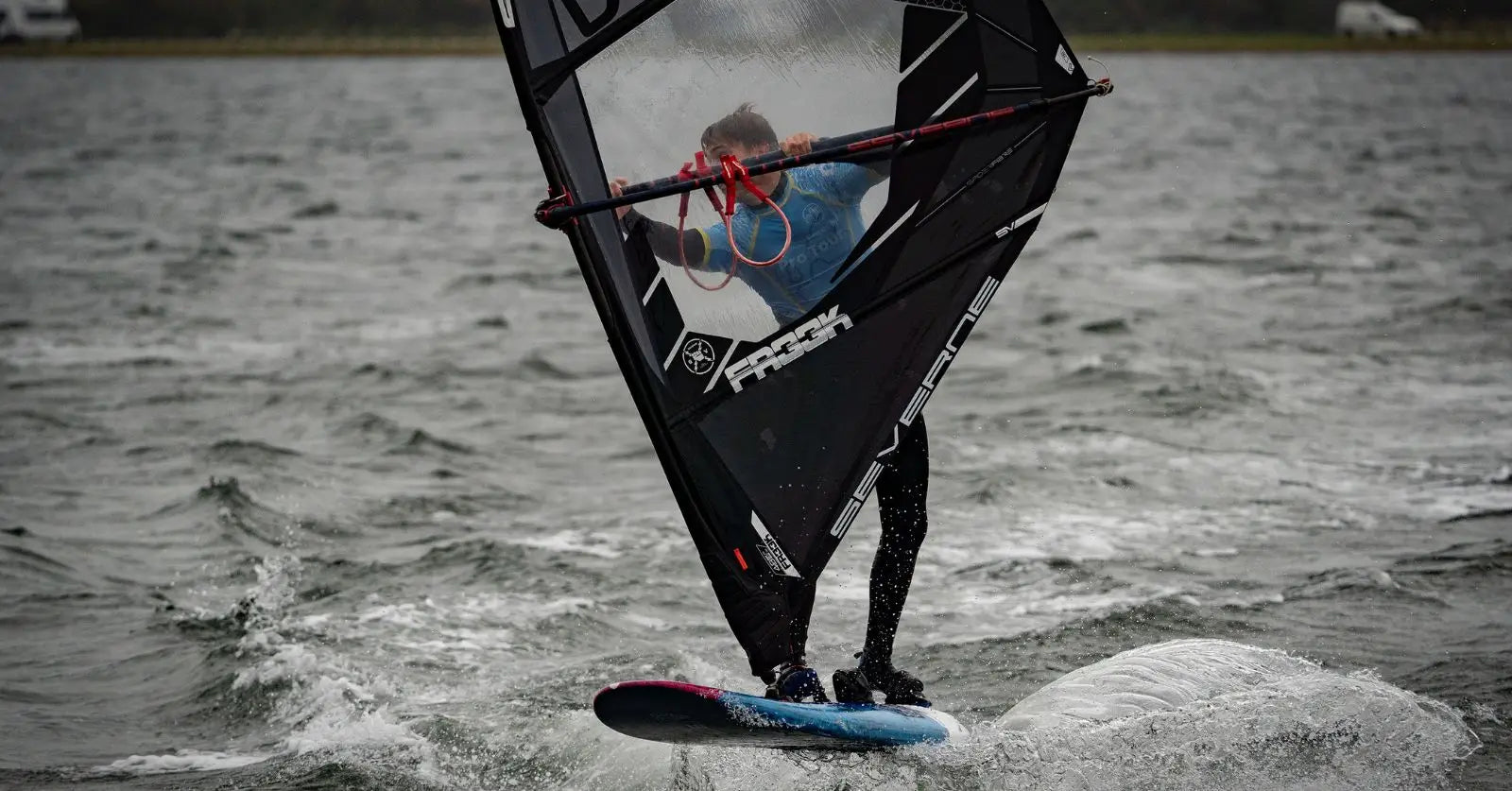 Performance windsurfing board with black sail and blue bottom in freezing Denmark session