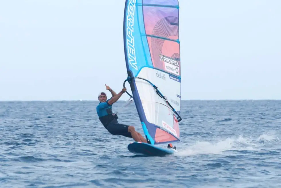 Windsurfer flying on flatwater with blue white sail, black shorts, teal top