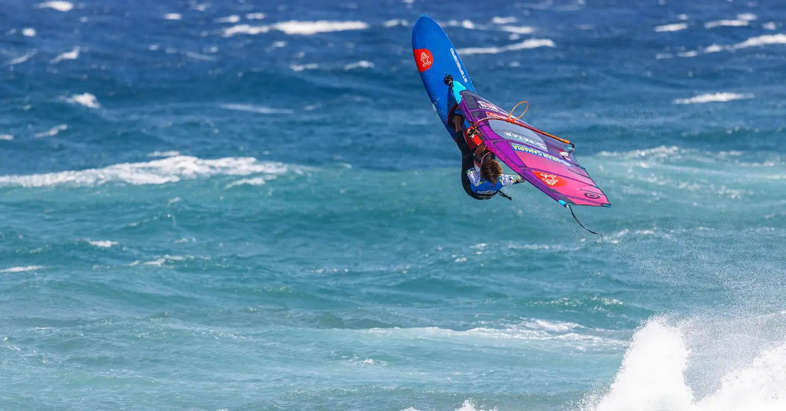Sarah-Quita on blue windsurfing board with colorful graphics and purple fins in Pozo