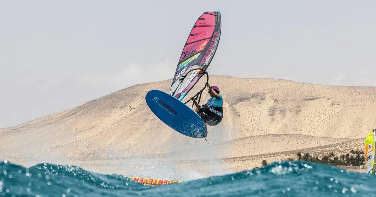 Performance windsurfing board with colorful sail and blue fin at PWA Fuerteventura World Cup