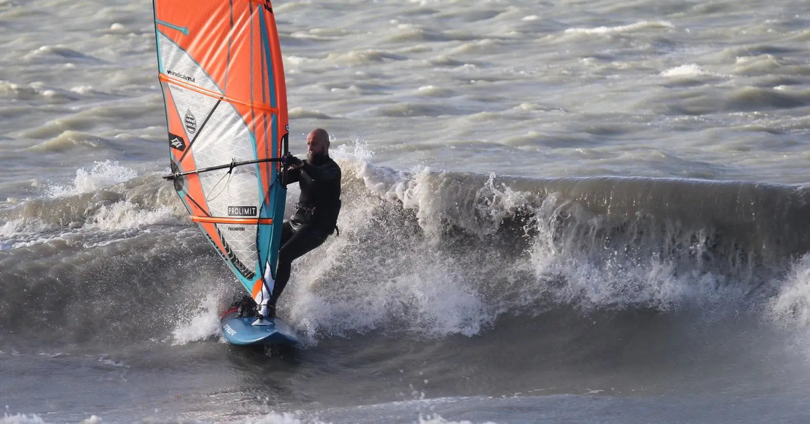 Orange and white Starboard Ultra windsurfing sail with black harness