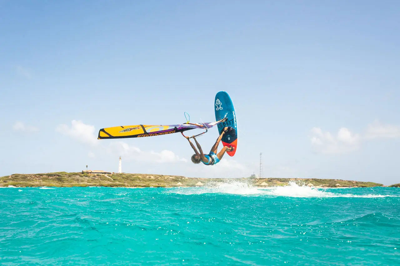 Starboard iGnite windsurfing board with yellow-blue design, black fins, carbon fiber.