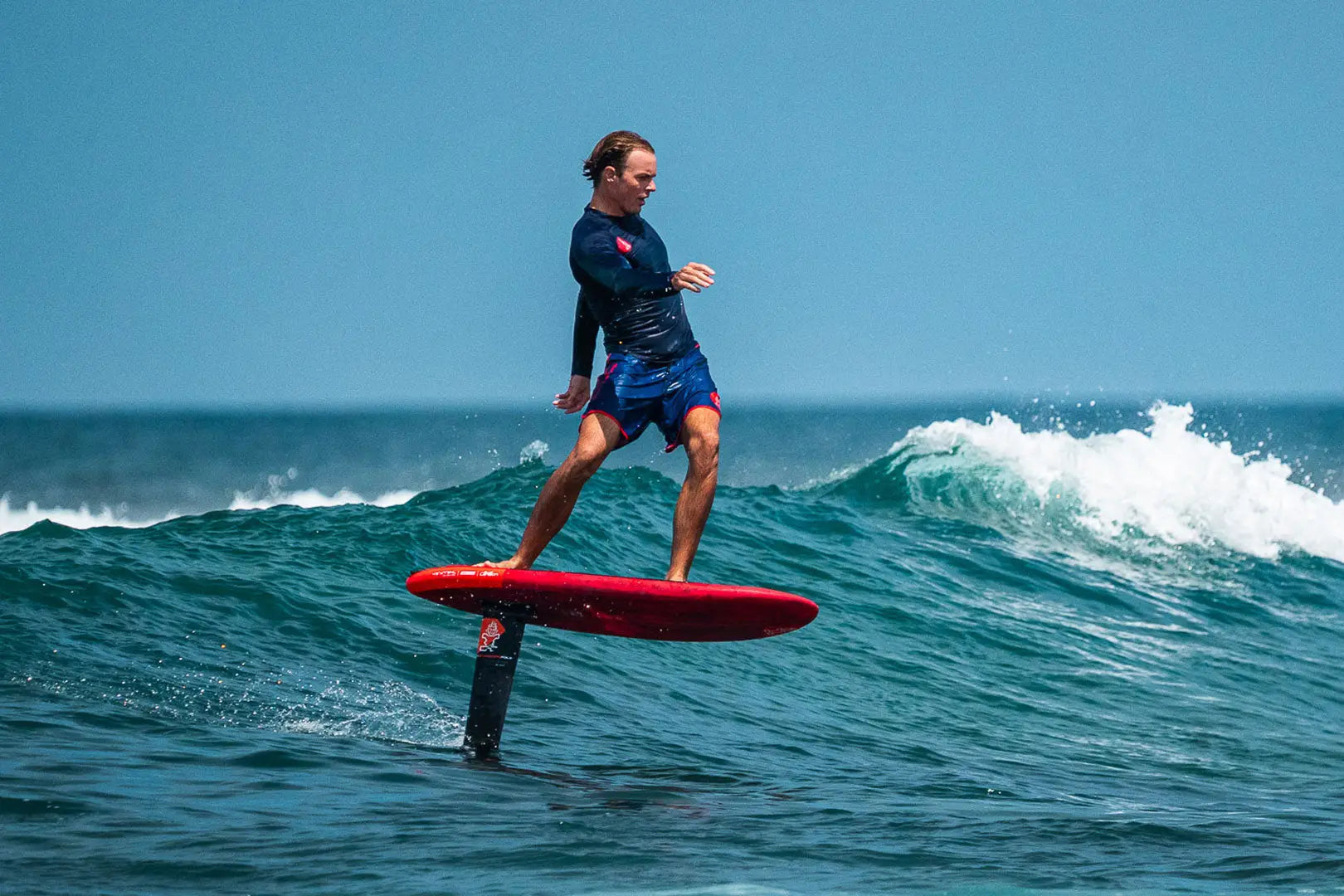 Red hydrofoil board with black fins and blue leash for water sports.