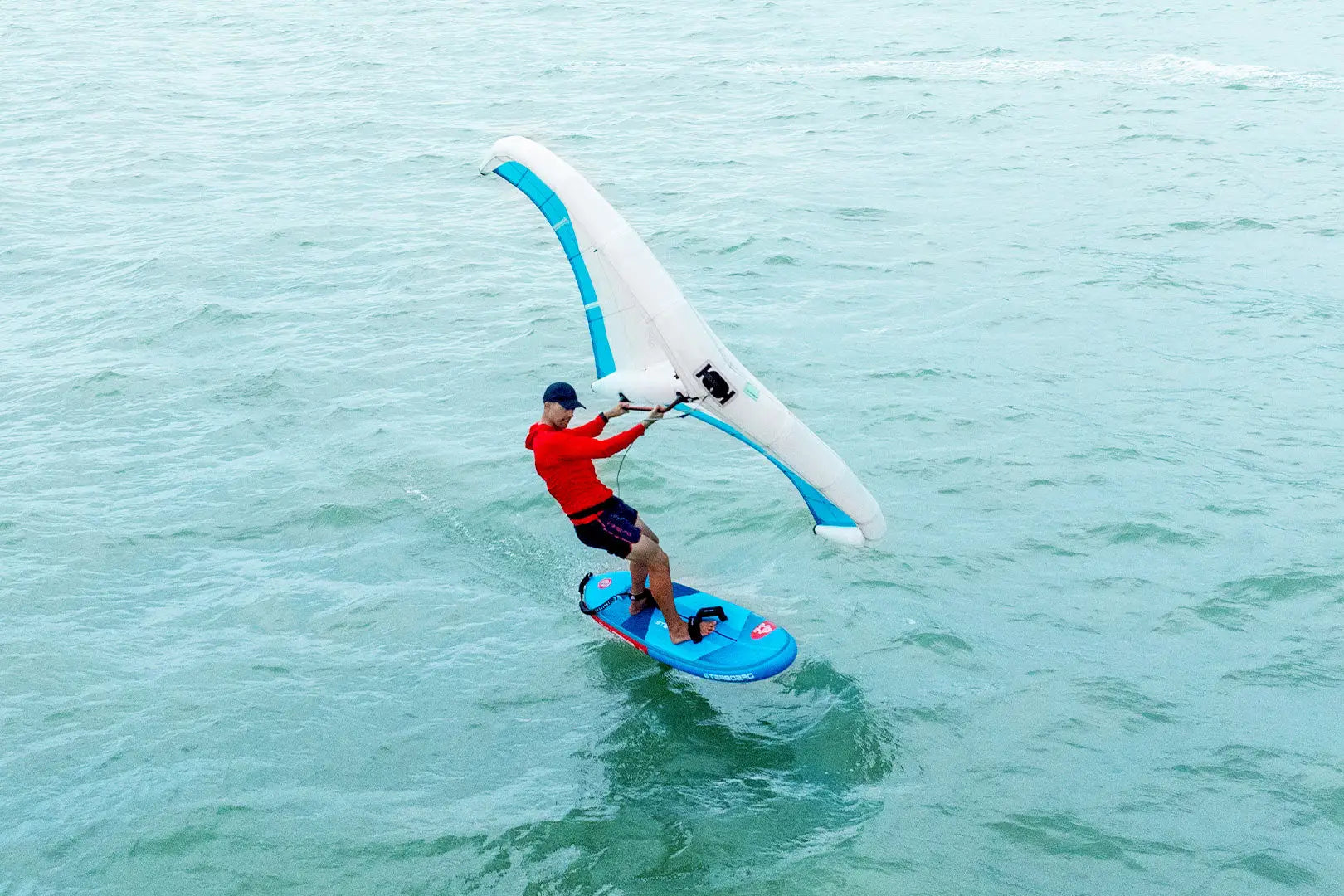 Blue windsurfing board with white teal sail for recreational use