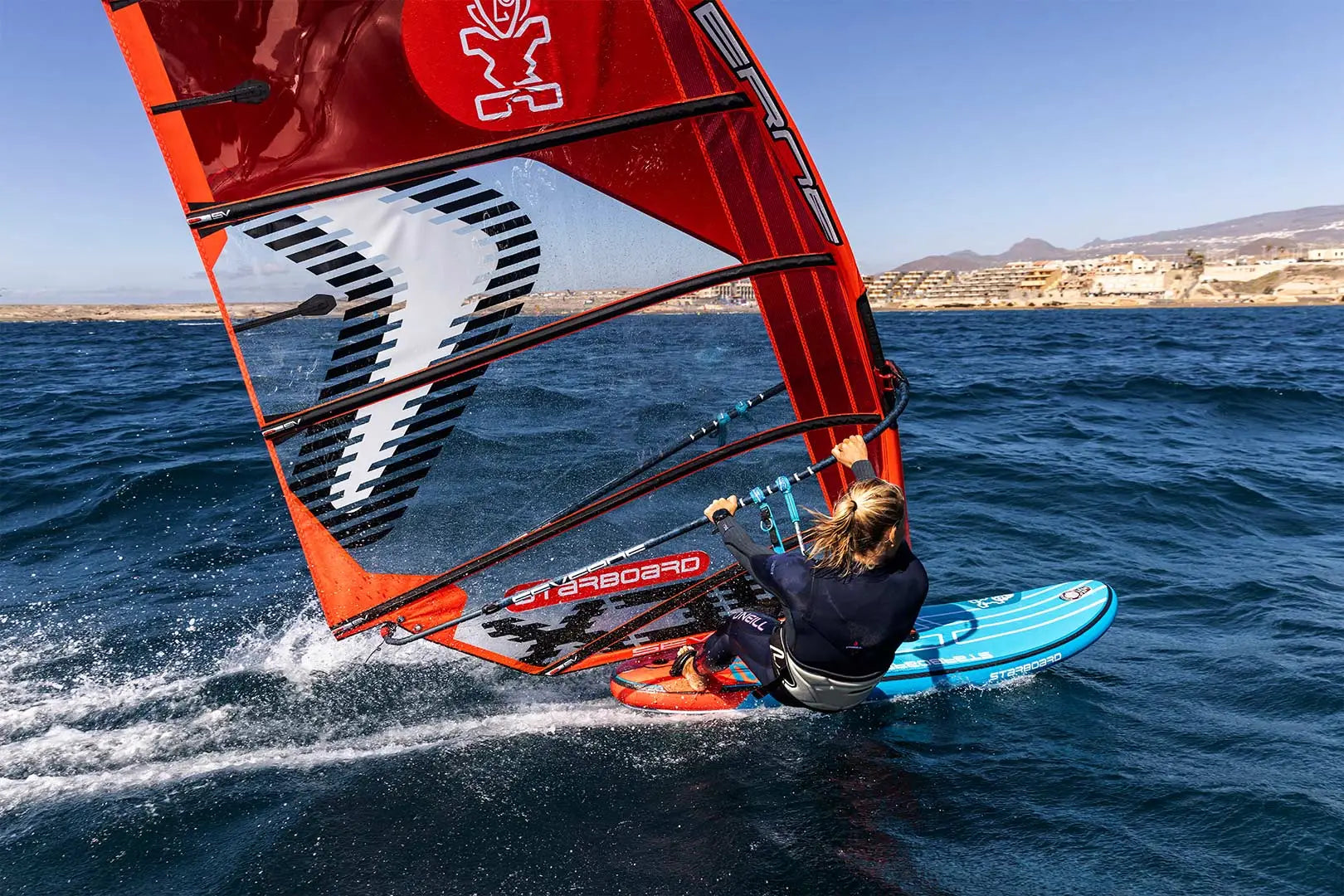 Red and black windsurfing sail with white logo on blue inflatable board
