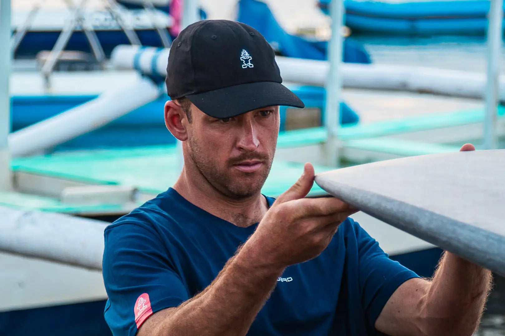 Navy blue long-sleeved shirt with white logo, black cap, gray surfboard