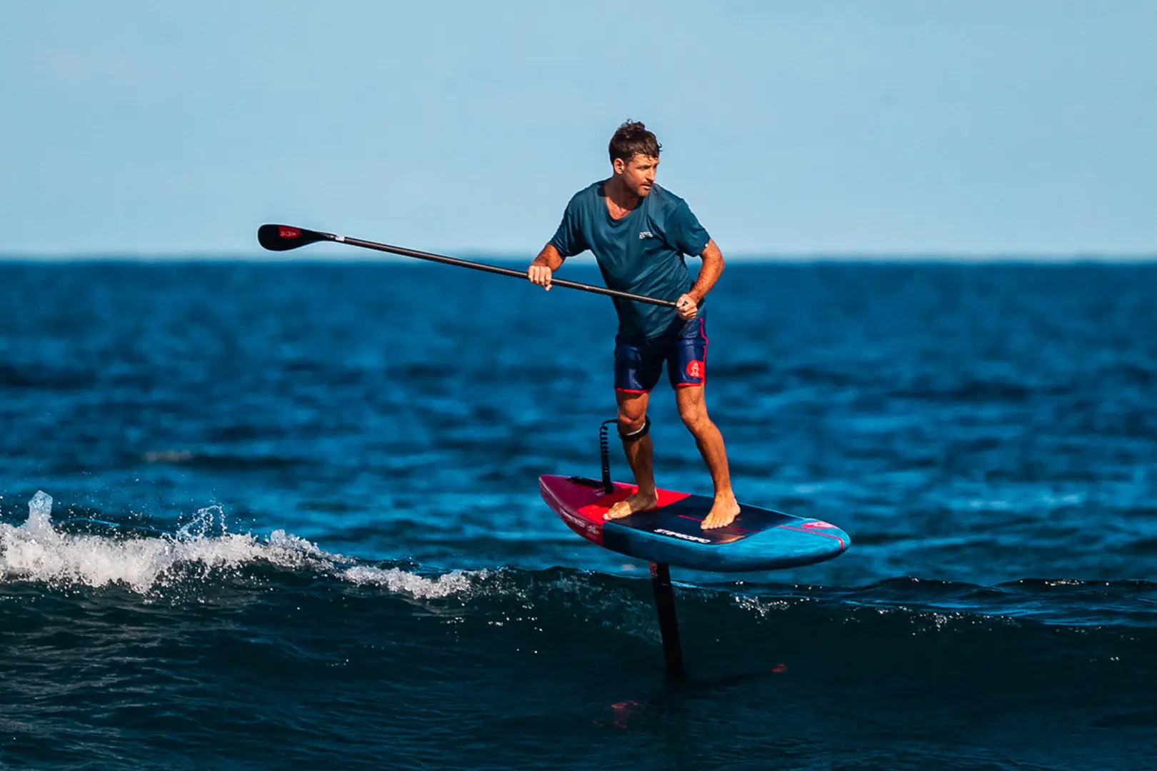 Blue and red hydrofoil paddleboard with black handlebars for downwind foil