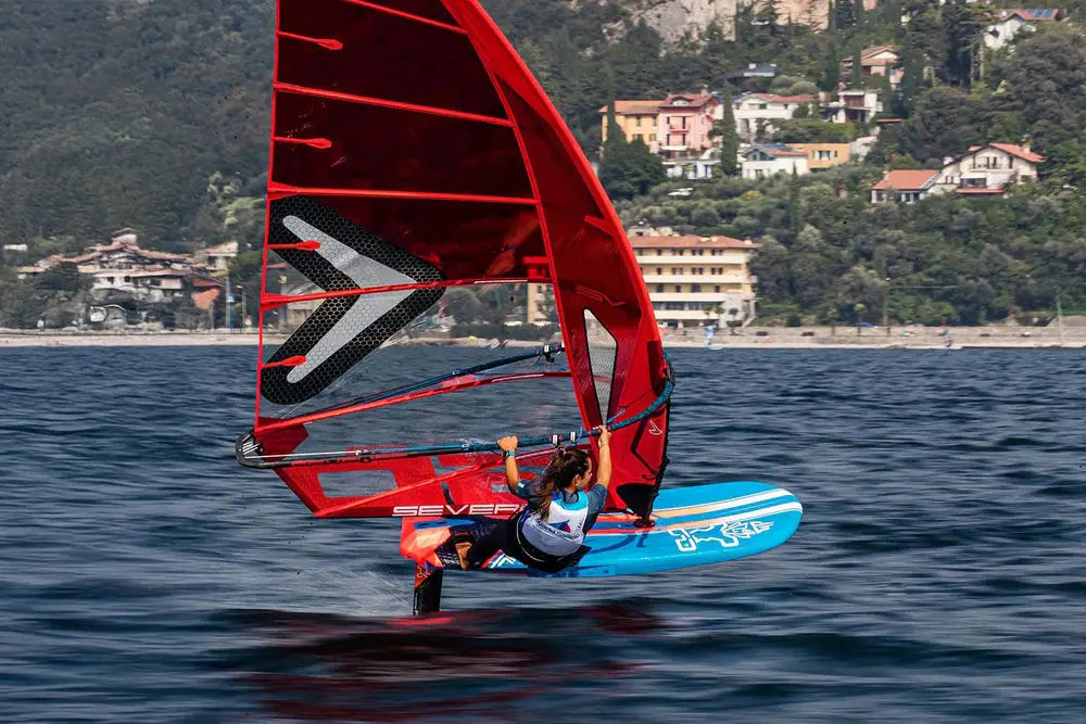 Red and black iQFOiL windsurfing board with blue sail for recreational use