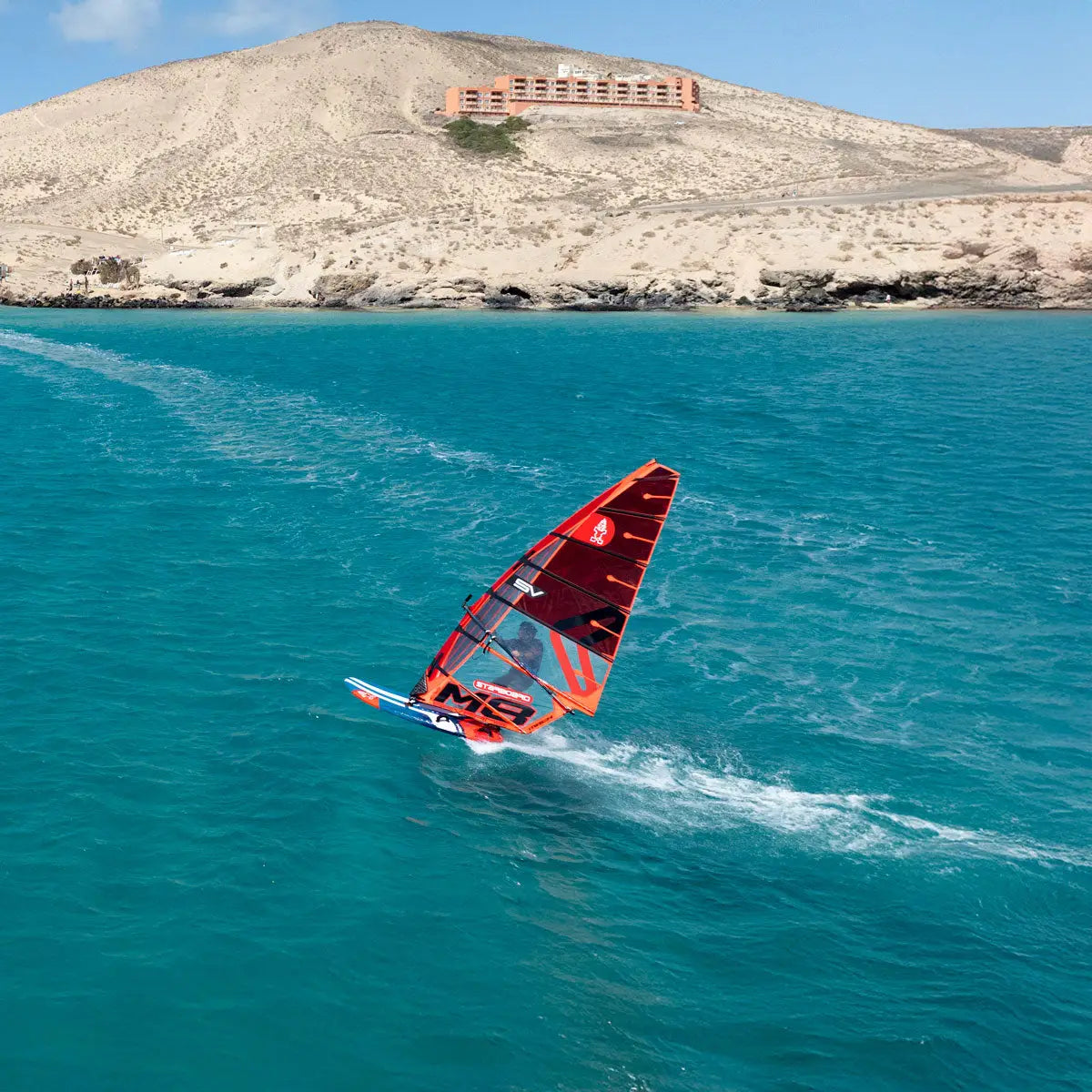 High-performance iSonic red windsurf board with white sail and orange accents.