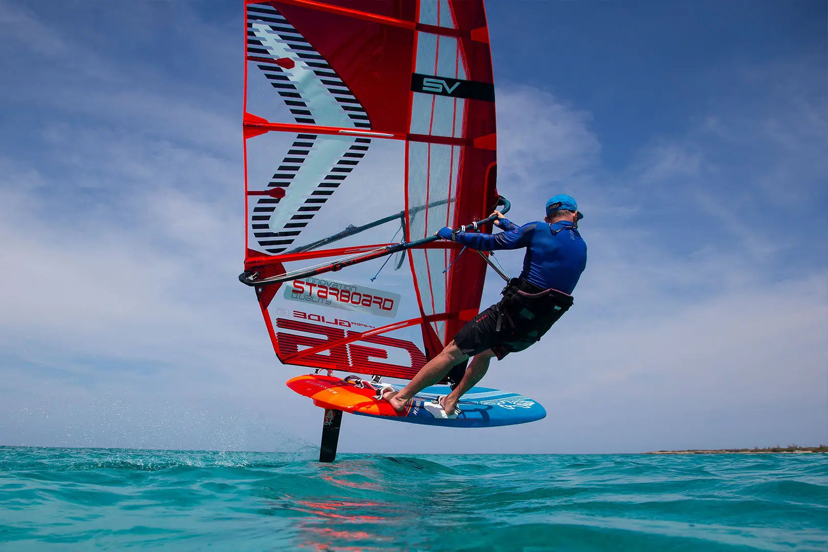 Red and white starboard sail with orange trim on blue Millennium Windfoil Board