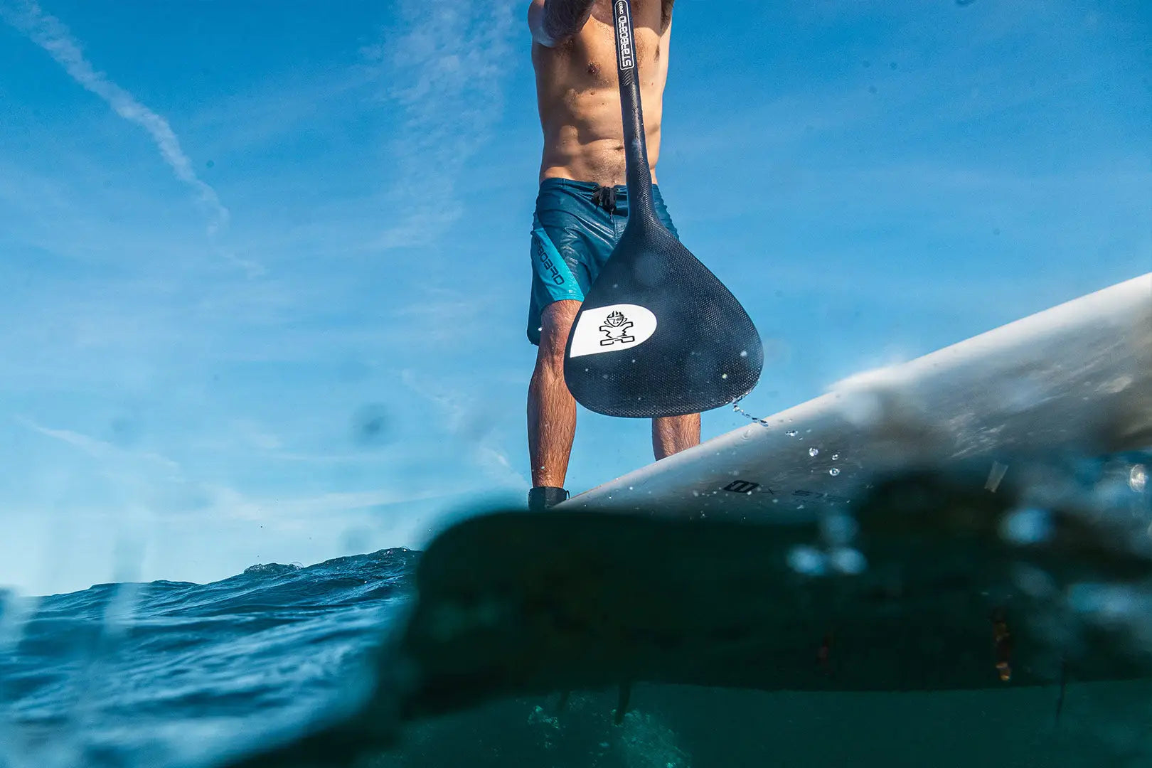 Stand-up paddleboard with black and white design in clear water, blue shorts, SUP Paddles collection