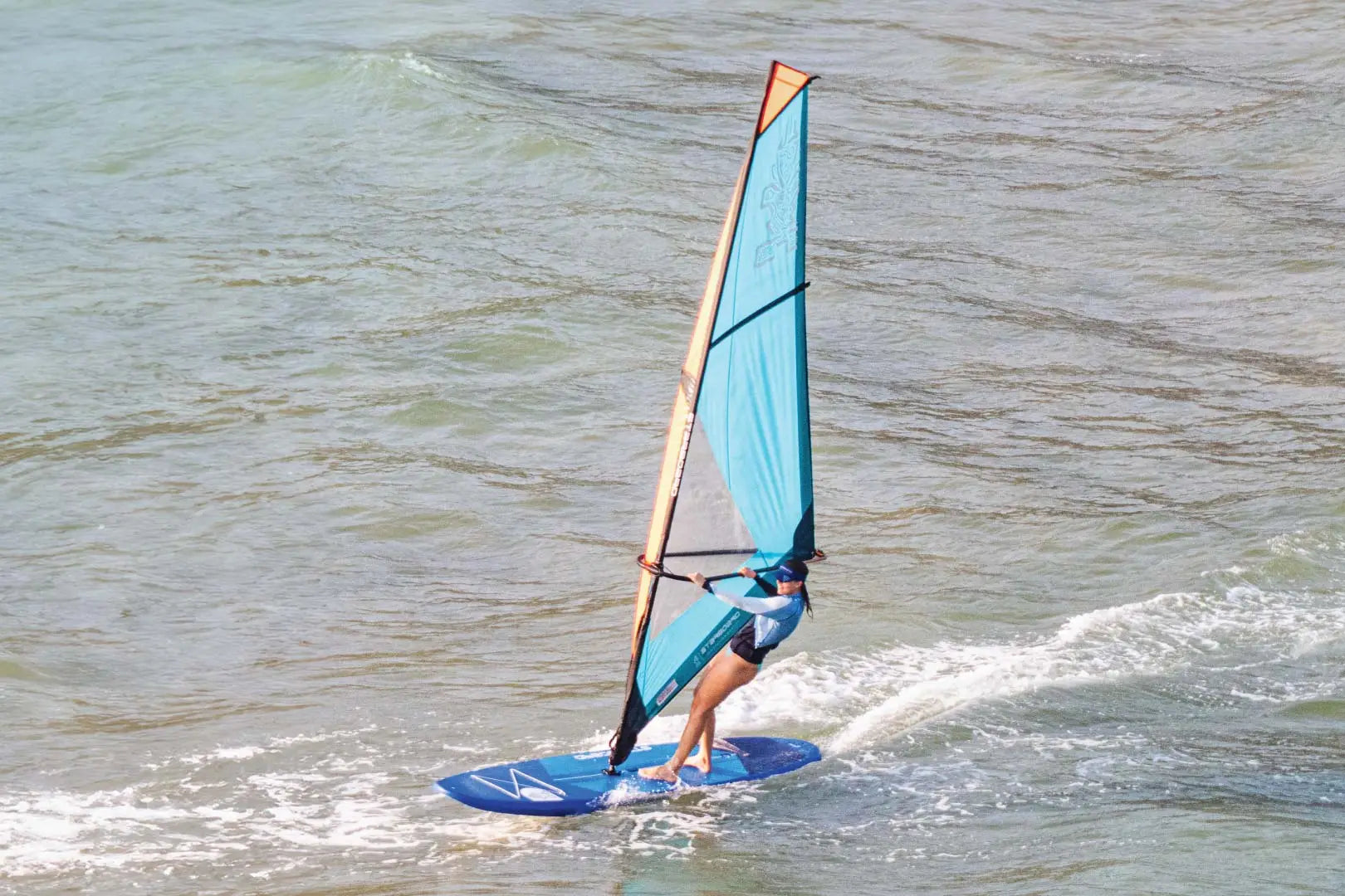 Blue windsurfing board with sail and leash for recreational use