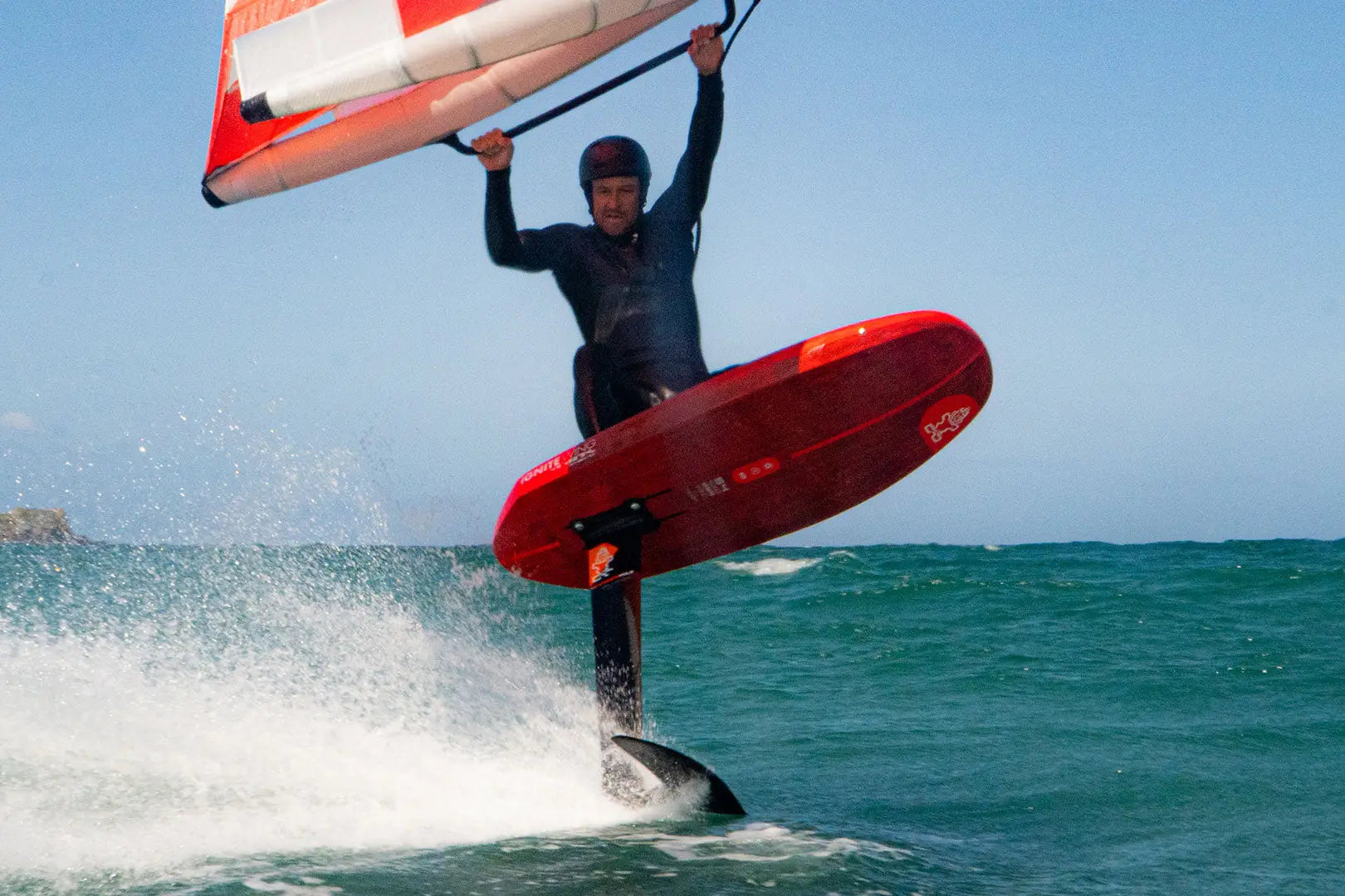 Red hydrofoil wing foil board with black fins and white sail