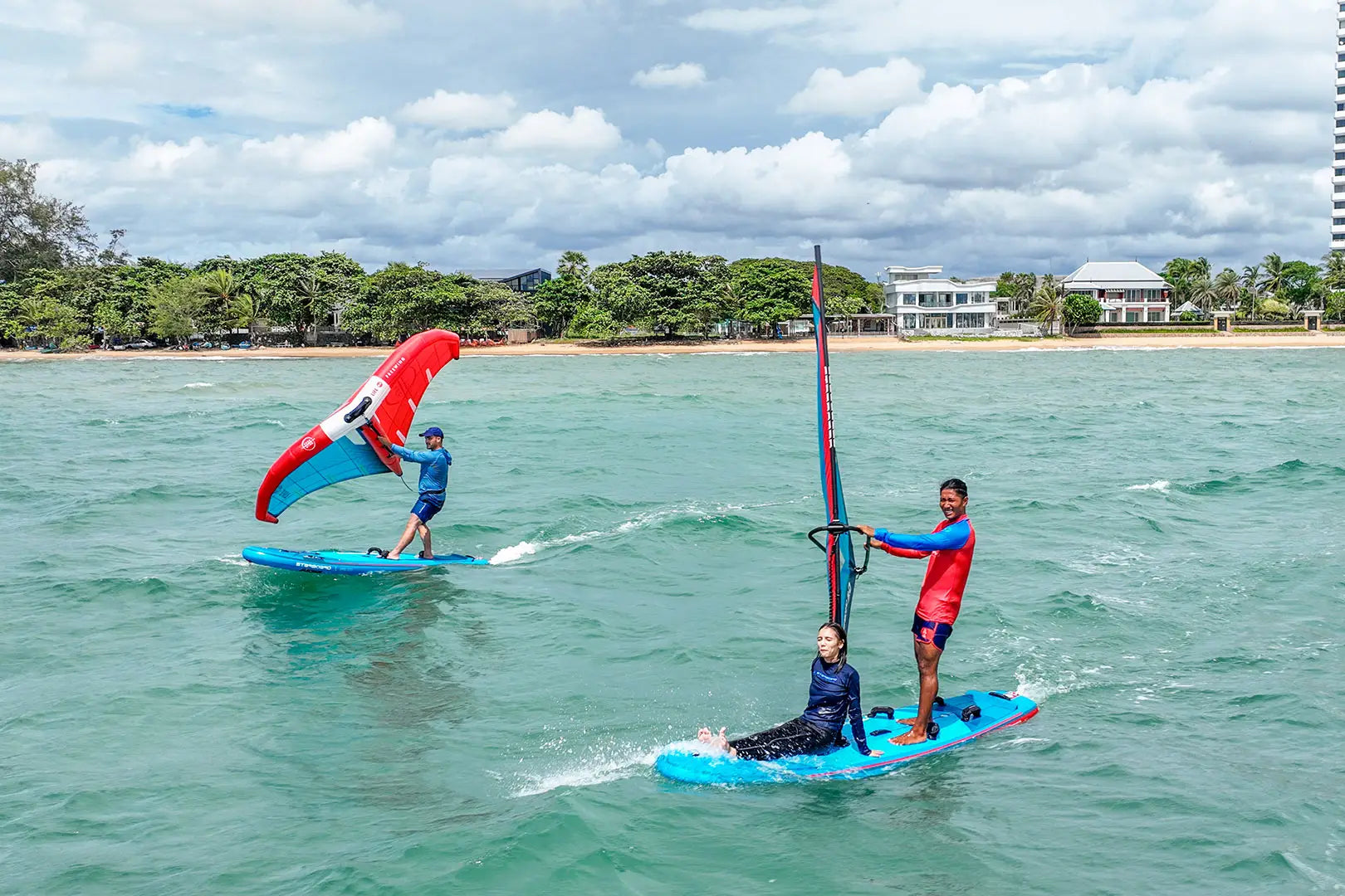 Blue fiberglass windsurfing board with red sail and white trim
