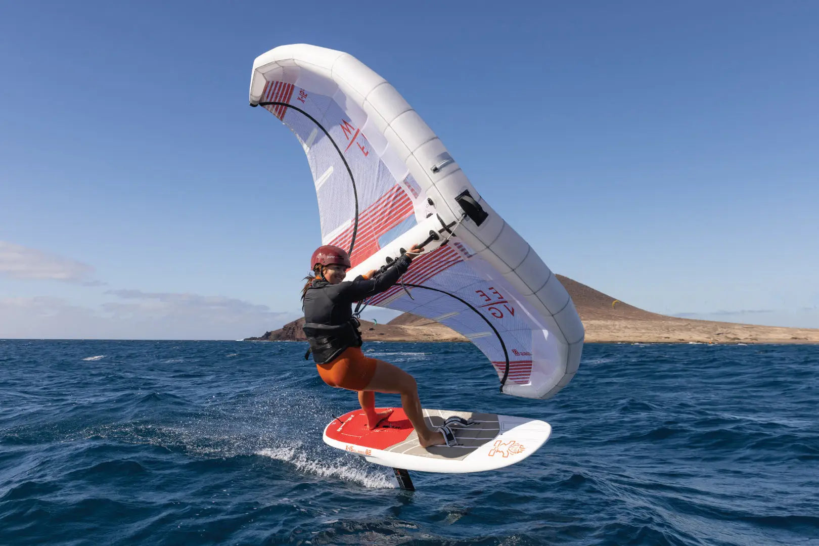 X-15 Foilboards windsurfing board with red white sail orange fins black harness blue water